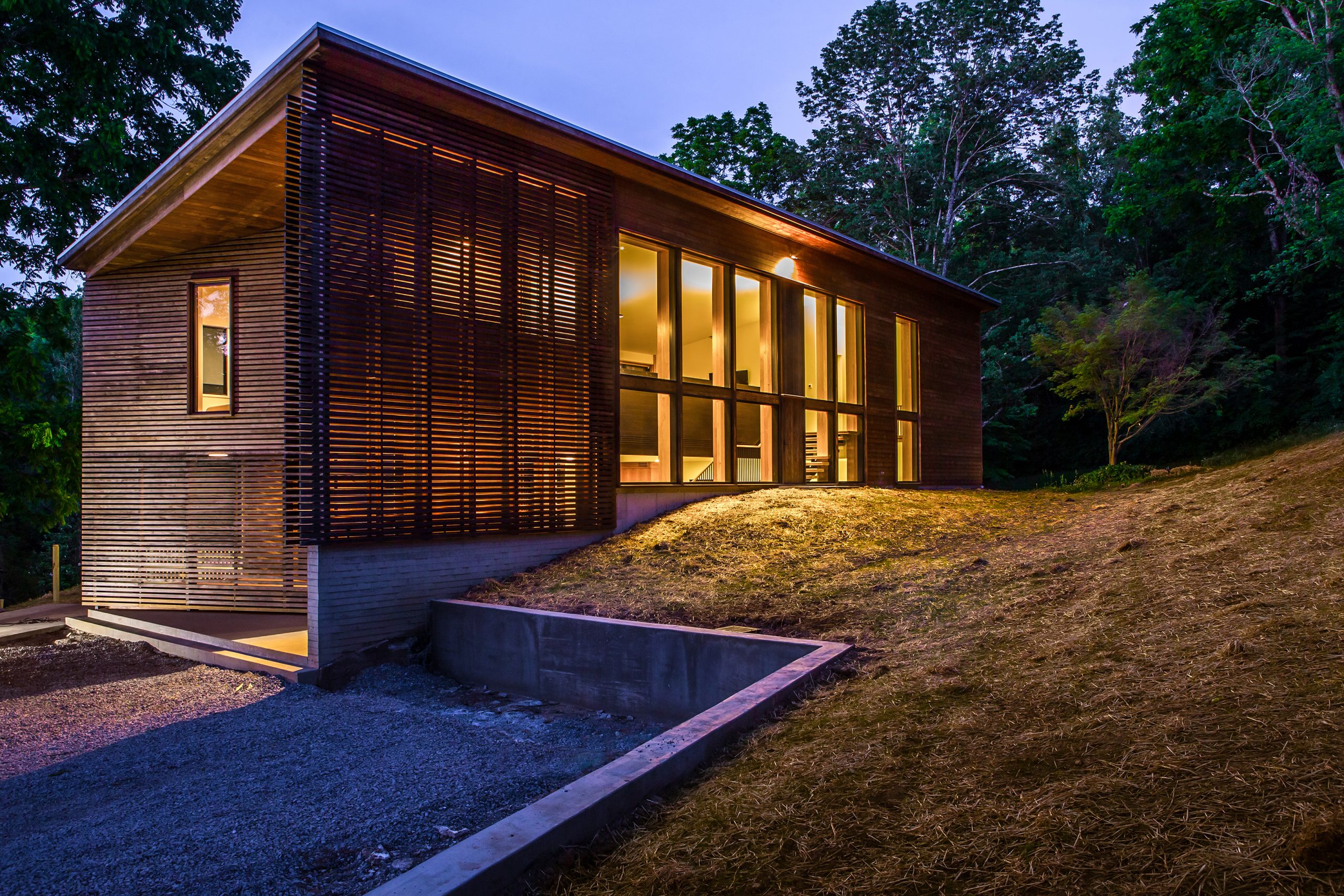 Exterior side view of the stone path leading to the entrance of Wood Screen House in Nashville, Tennessee during nighttime and featuring Kebony Modified Wood Clear Cladding