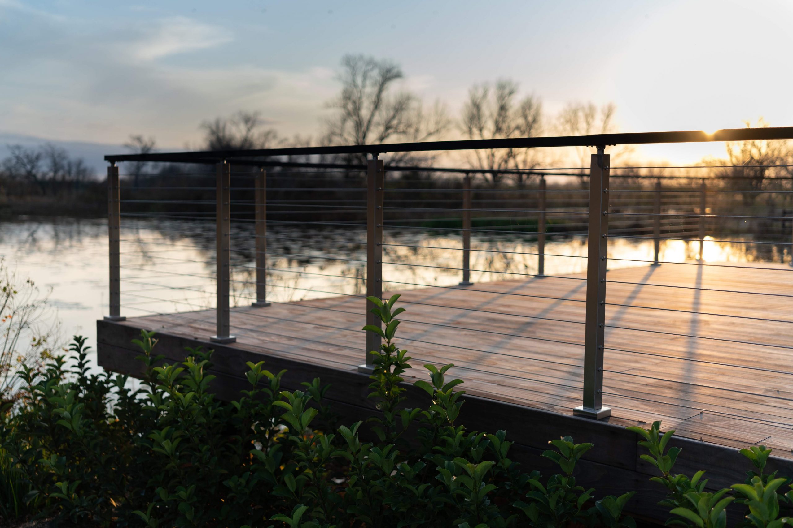 View overlooking the pond from the patio deck at the Fulshear Modern Ranch Estate featuring Kebony Modified Wood Character Decking in Fulshear, Texas during a sunset
