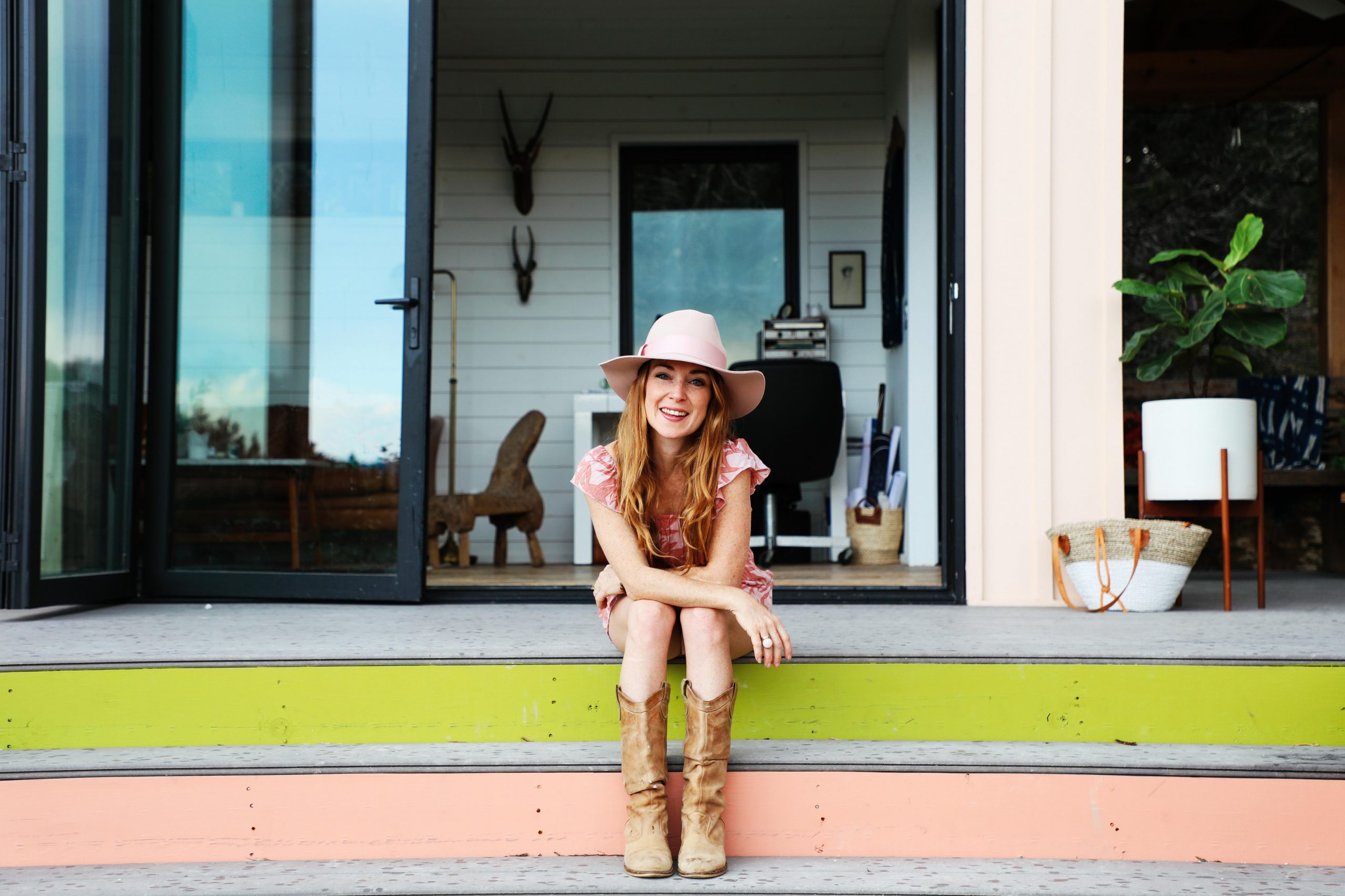 Kim Lewis smiles while sitting on the steps of her Peached Casita Home featuring Kebony Modified Wood Step-Clip Boarding on a sunny day and located in Dripping Springs, Texas