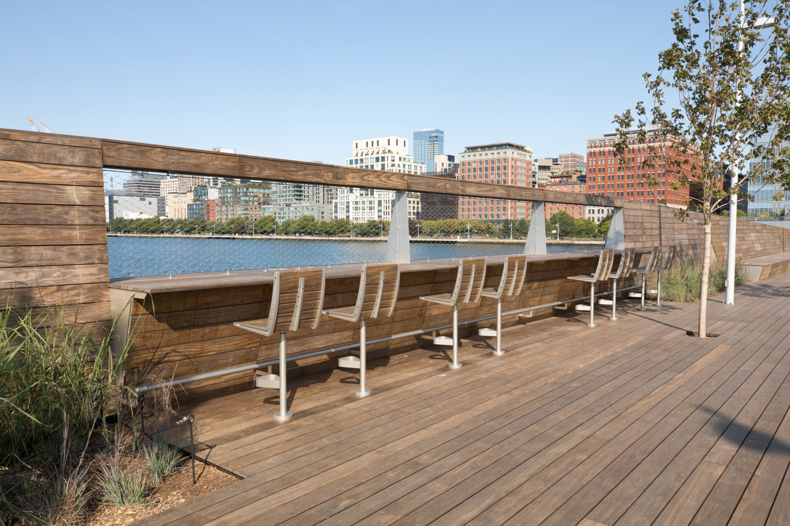 Three sets of two barstools with a half bar top over-looking the Hudson River at Pier 26 during the day at Hudson River Park in New York City New York features kebony modified wood Clear Boardwalk Decking.