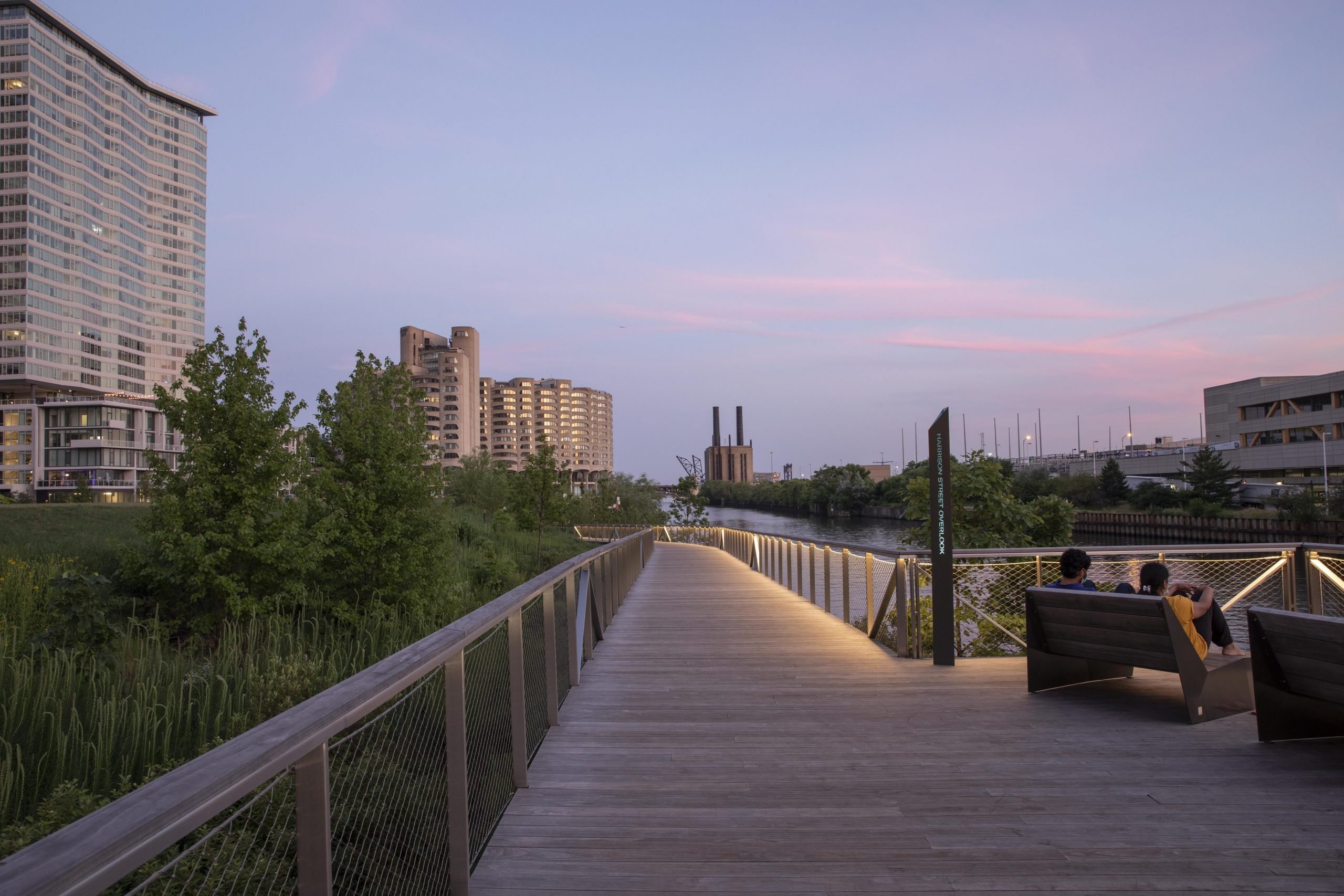 View of Kebony Modified Wood Clear Decking boardwalk on the Southbank Riverwalk in Chicago Illinois at dusk being lit up by lights underneath the handrails