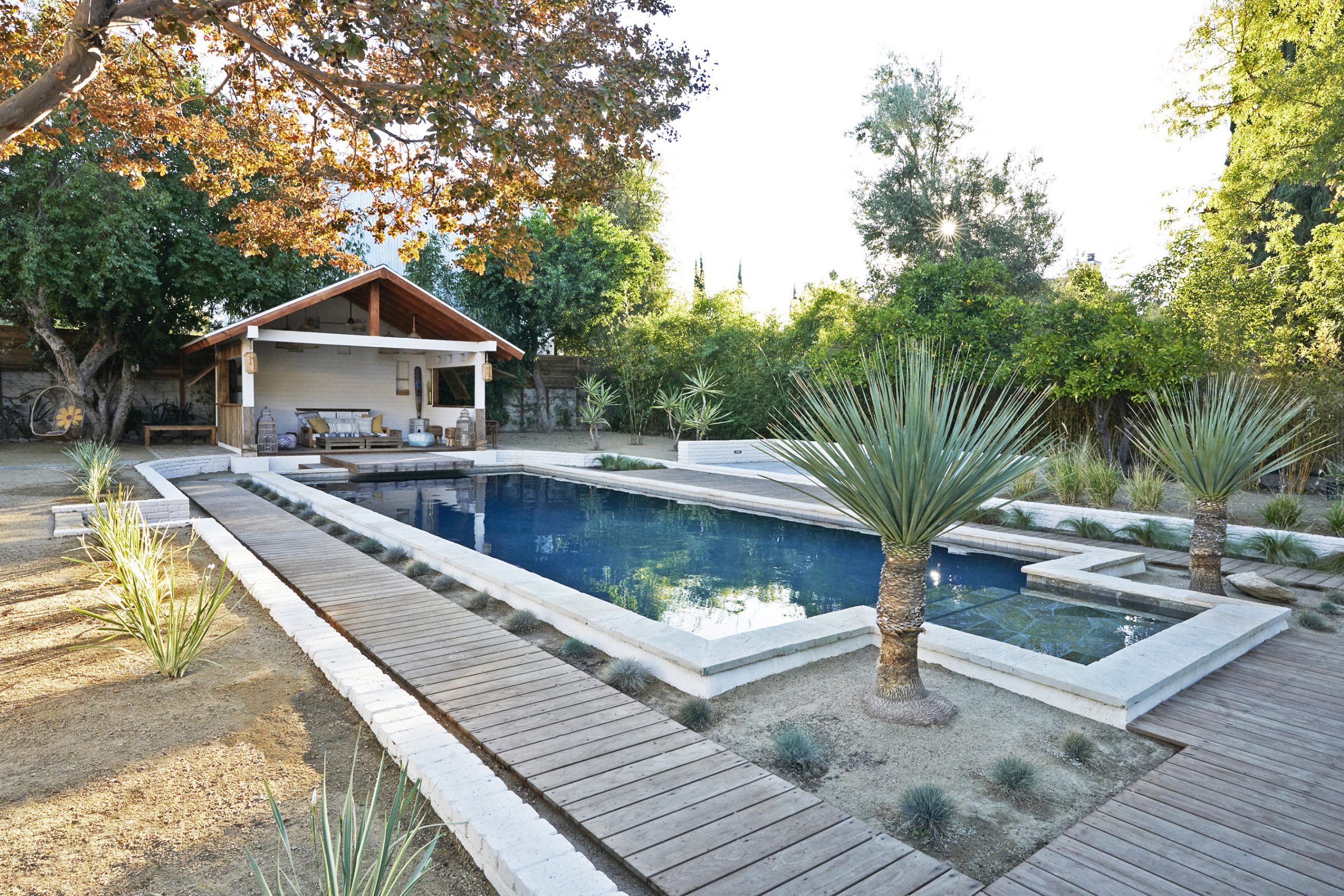 Three quarter's view of the backyard rectangular pool and pool house of the Rum Punch House in Los Angeles California featuring Kebony Modified Wood Clear Decking in the evening