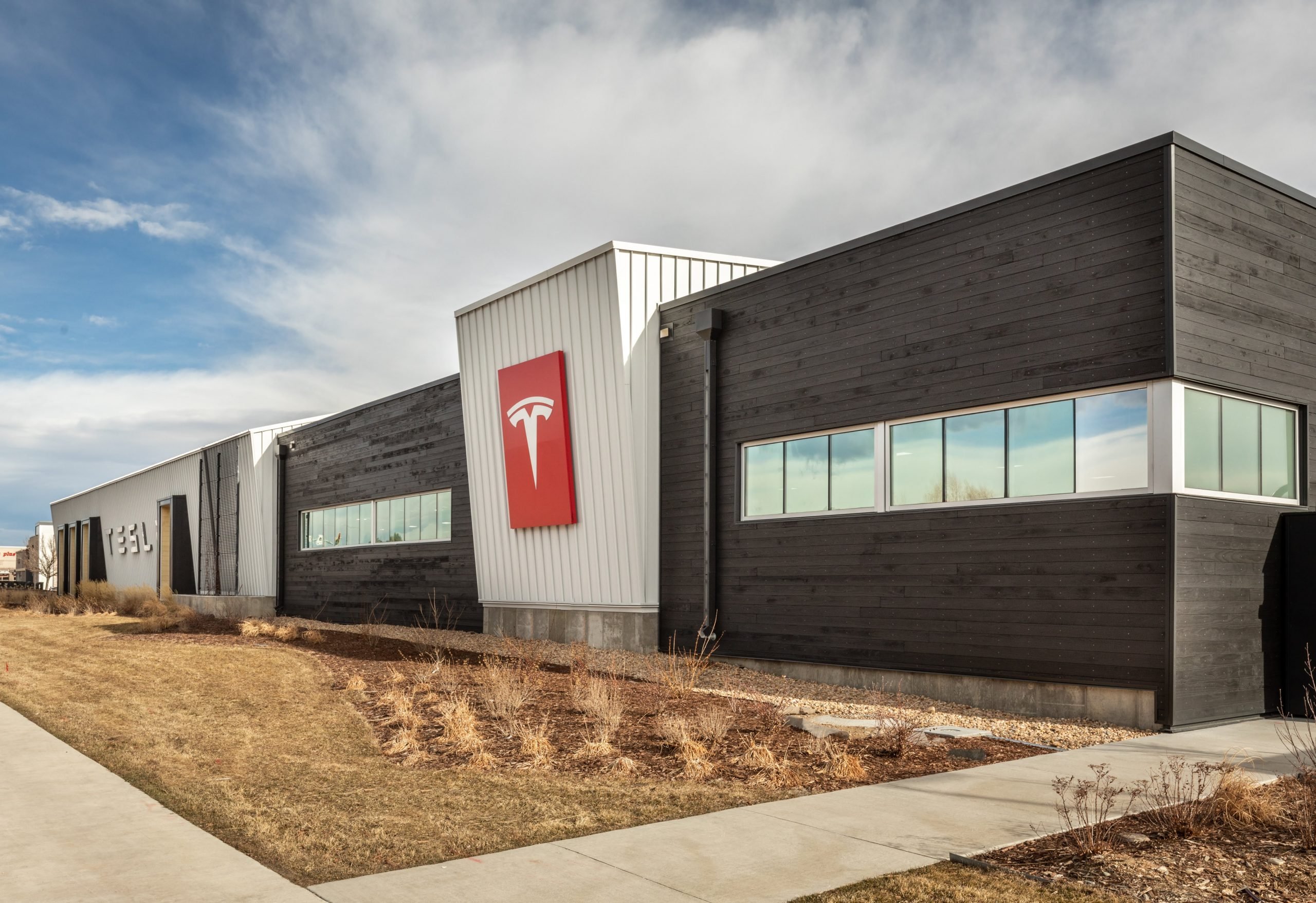 Three quarter's view of the Tesla Showroom in Denver Colorado features Kebony clear cladding with a red Tesla logo in the center and a cloudy sky in the background