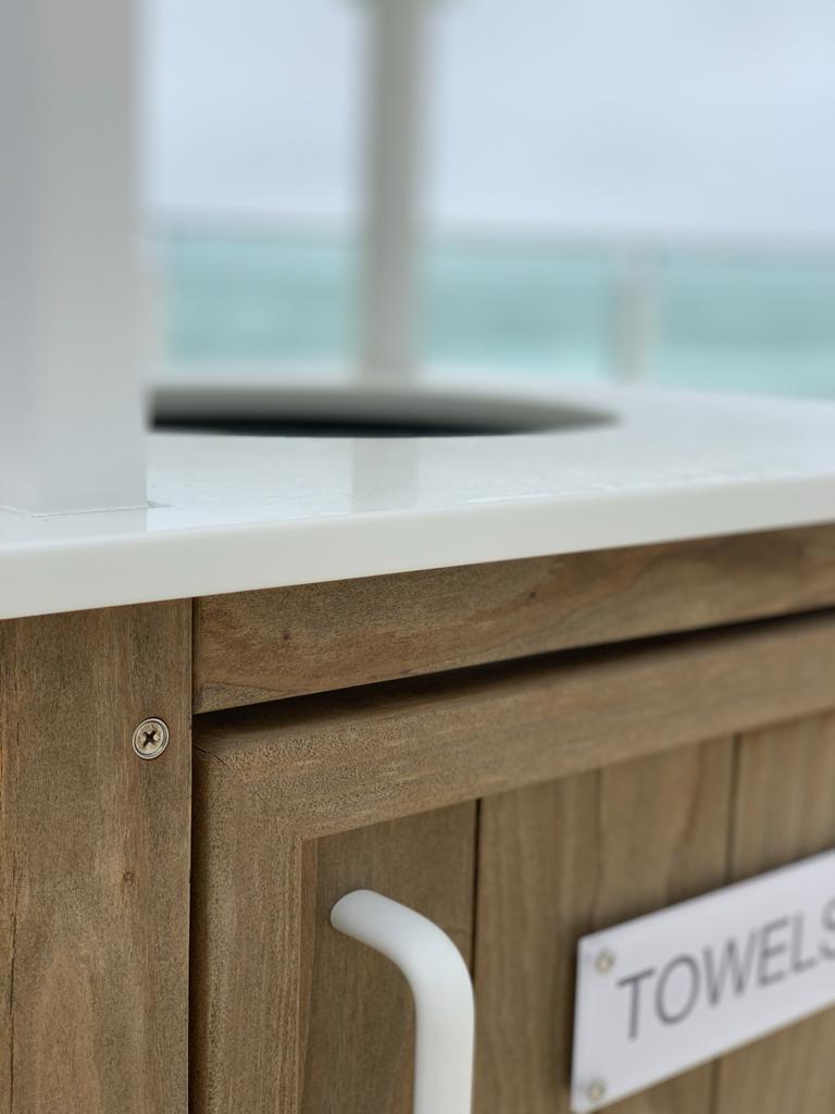 Close up of a CustomBeach towel bin featuring Kebony Modified Wood Clear Cladding during the day and overlooking the beautiful blue ocean and pristine beach in the background
