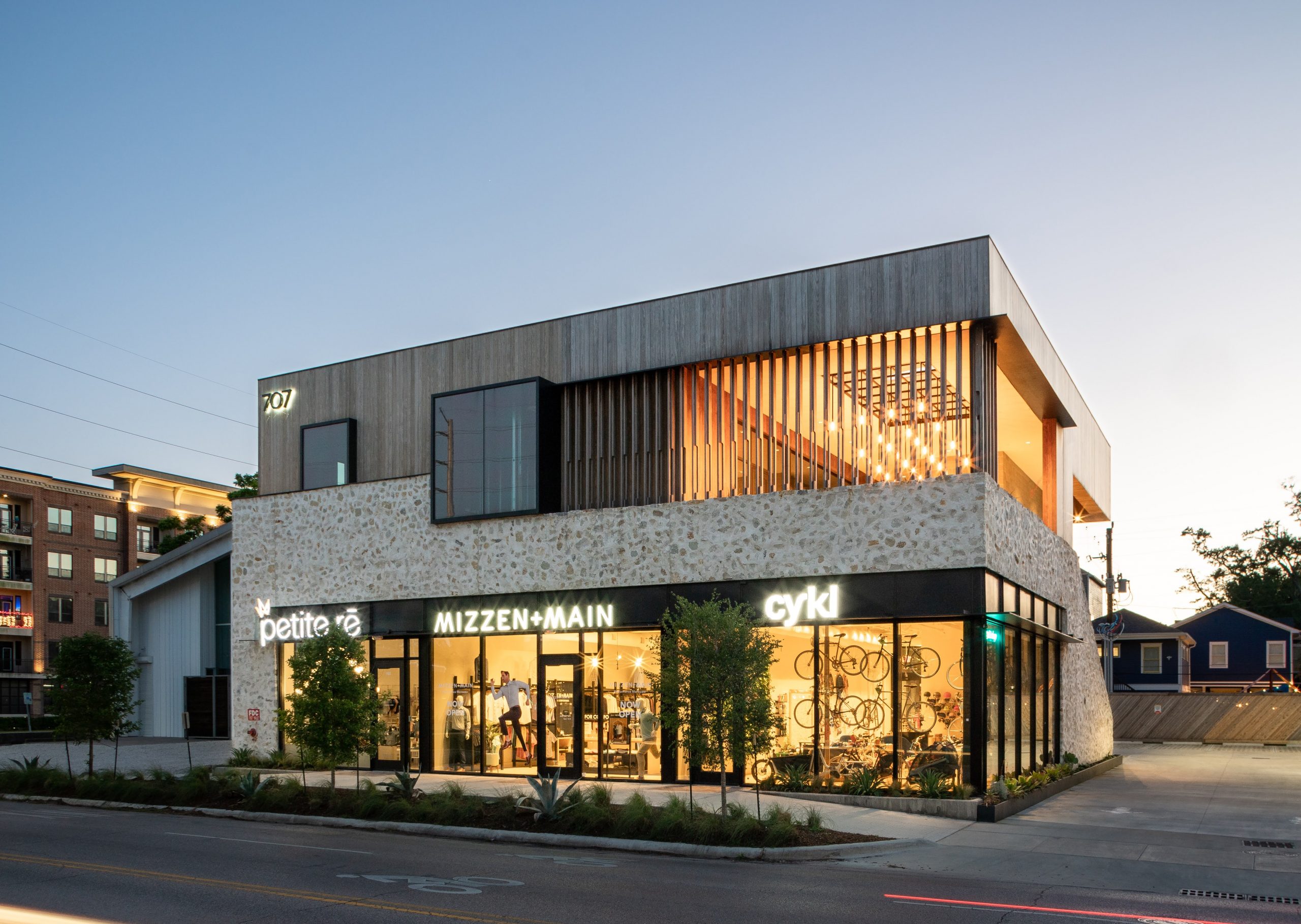 Outside view from the street of the 707 Yale Street Shops lit up at dusk in Houston Texas featuring Kebony modified wood clear cladding system