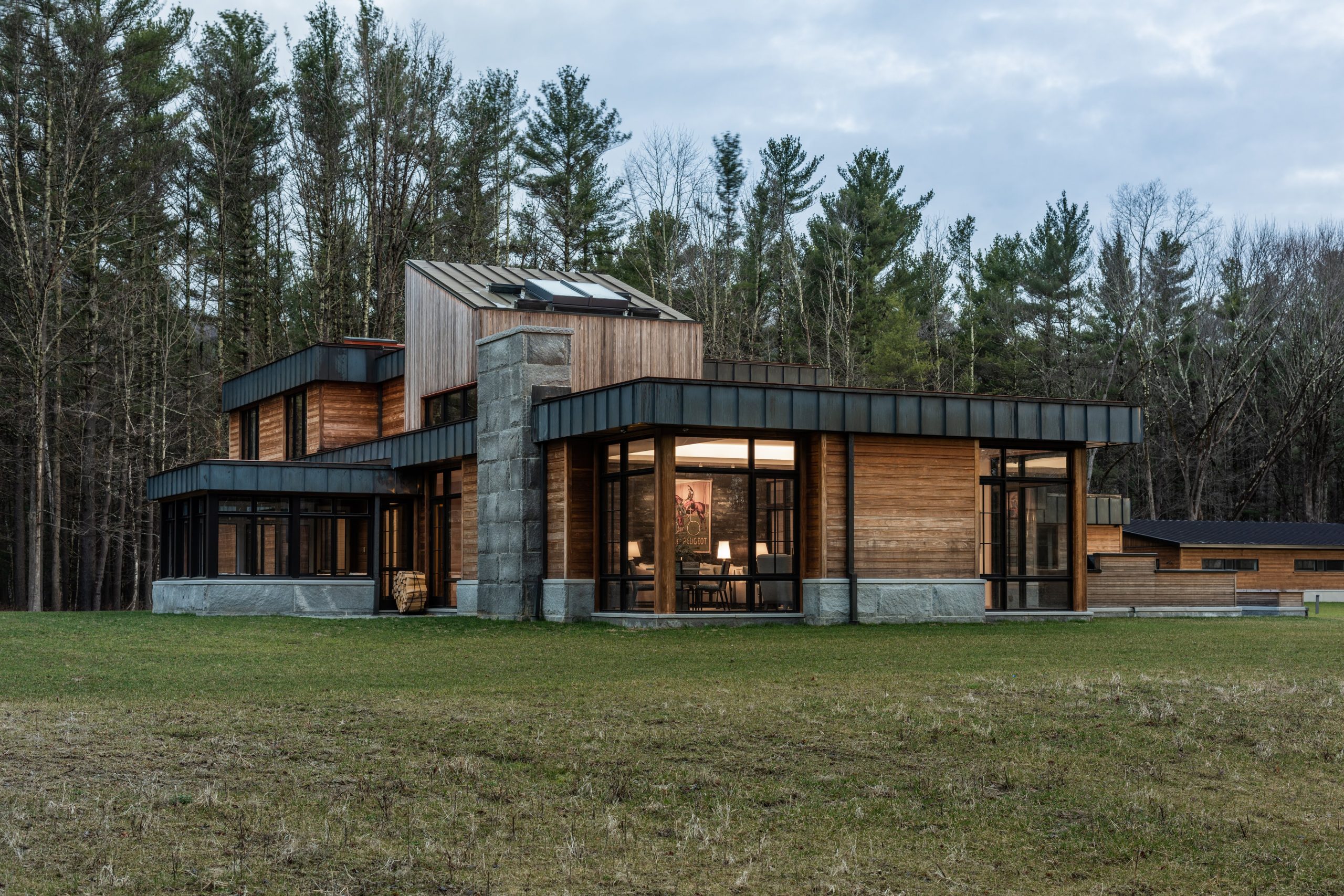 An outside three-quarter view of The Dower House on an overcast day nestled in a clearing with a wooded area in the background in Sheffield, Massachusetts and features Kebony Modified Wood Clear Cladding