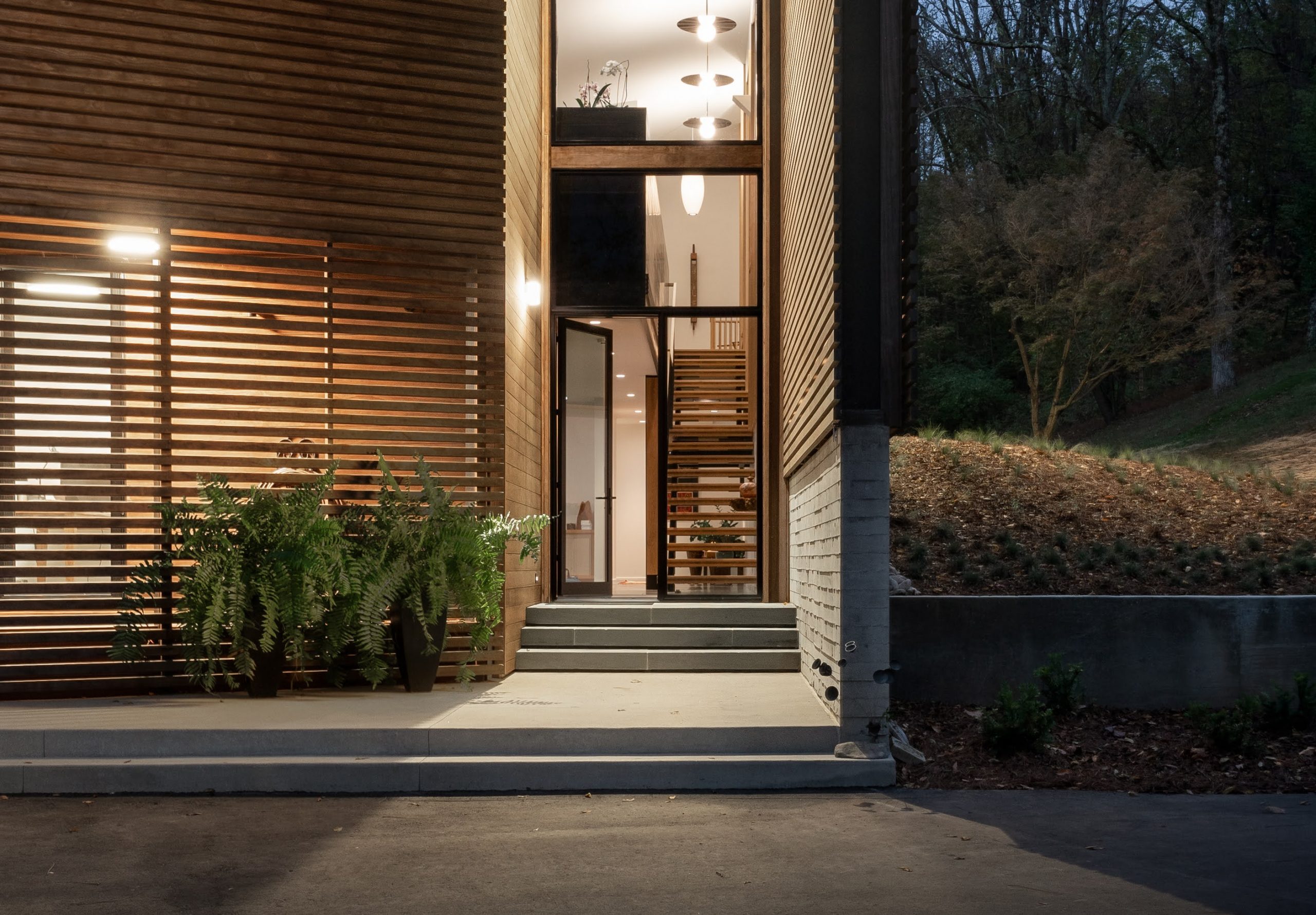 Exterior side view of the Wood Screen House in Nashville, Tennessee at night featuring Kebony Modified Wood Clear Cladding and minimal landscaping