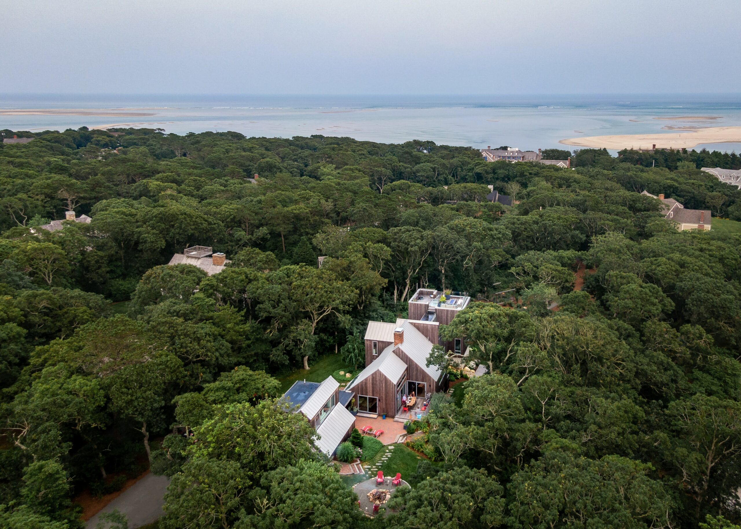 Morris Island Residence arial view with surrounding wooded area and Chatham Harbor on the horizon at Morris Island in Chatham, Massachusetts featuring Kebony Modified Wood Clear Cladding during the day