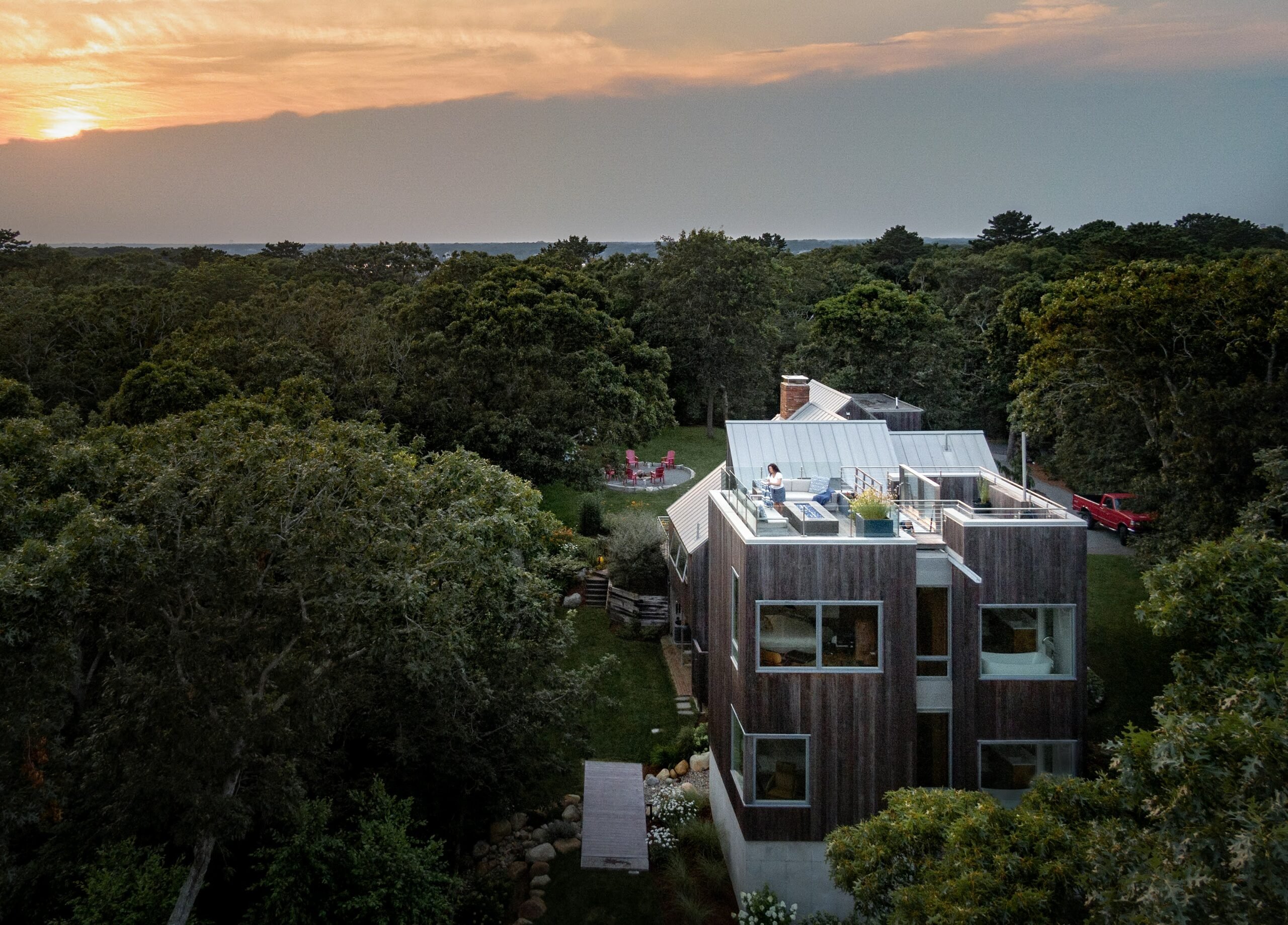 Arial view of the back of the house and a person on the rooftop looking at a beautiful sunset on Morris Island in Chatham, Massachusetts featuring Kebony Modified Wood Clear Cladding