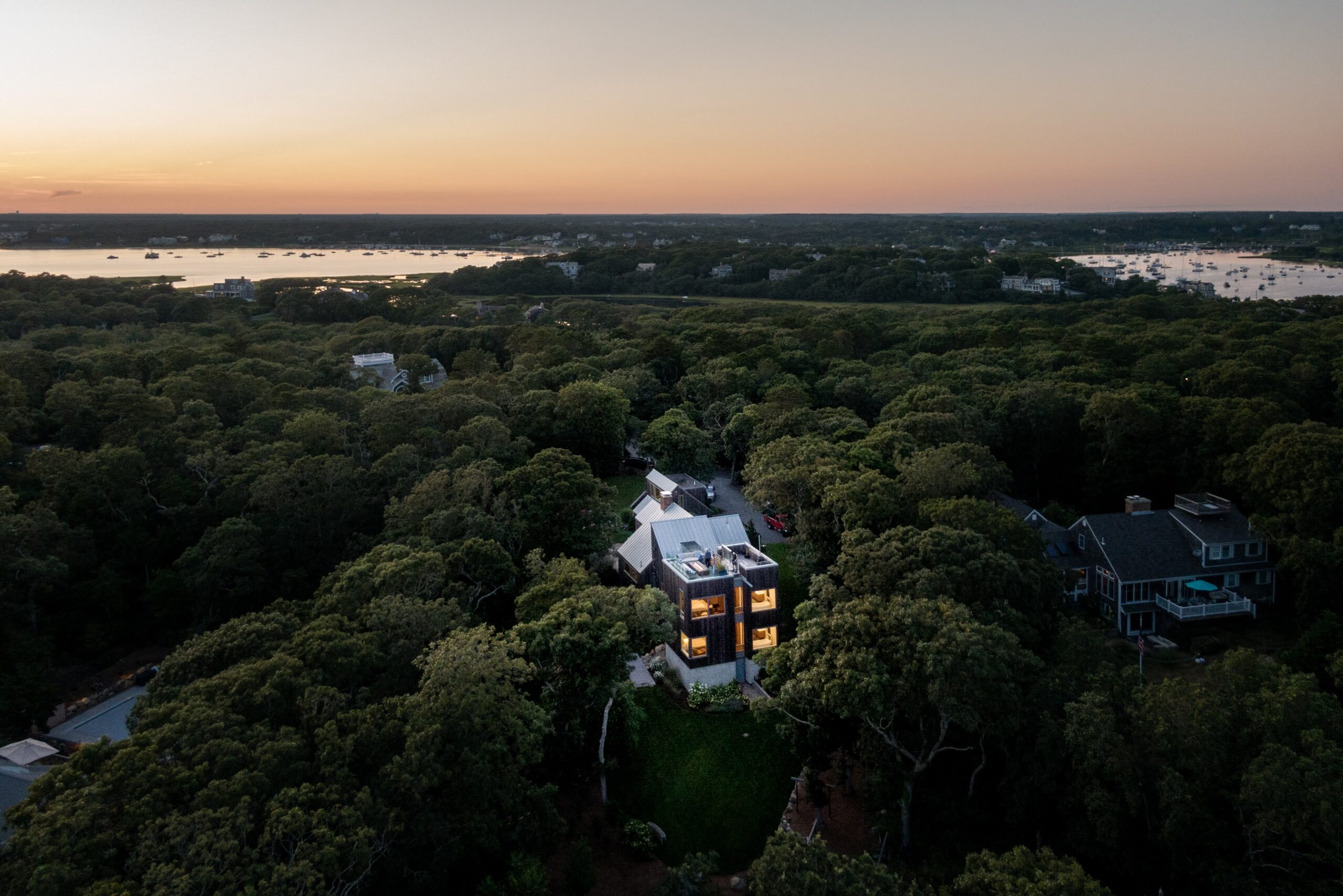 Arial view of the wooded area surrounding the warm windows during a beautiful sunset at Morris Island Residence on Morris Island in Chatham, Massachusetts featuring Kebony Modified Wood Clear Cladding