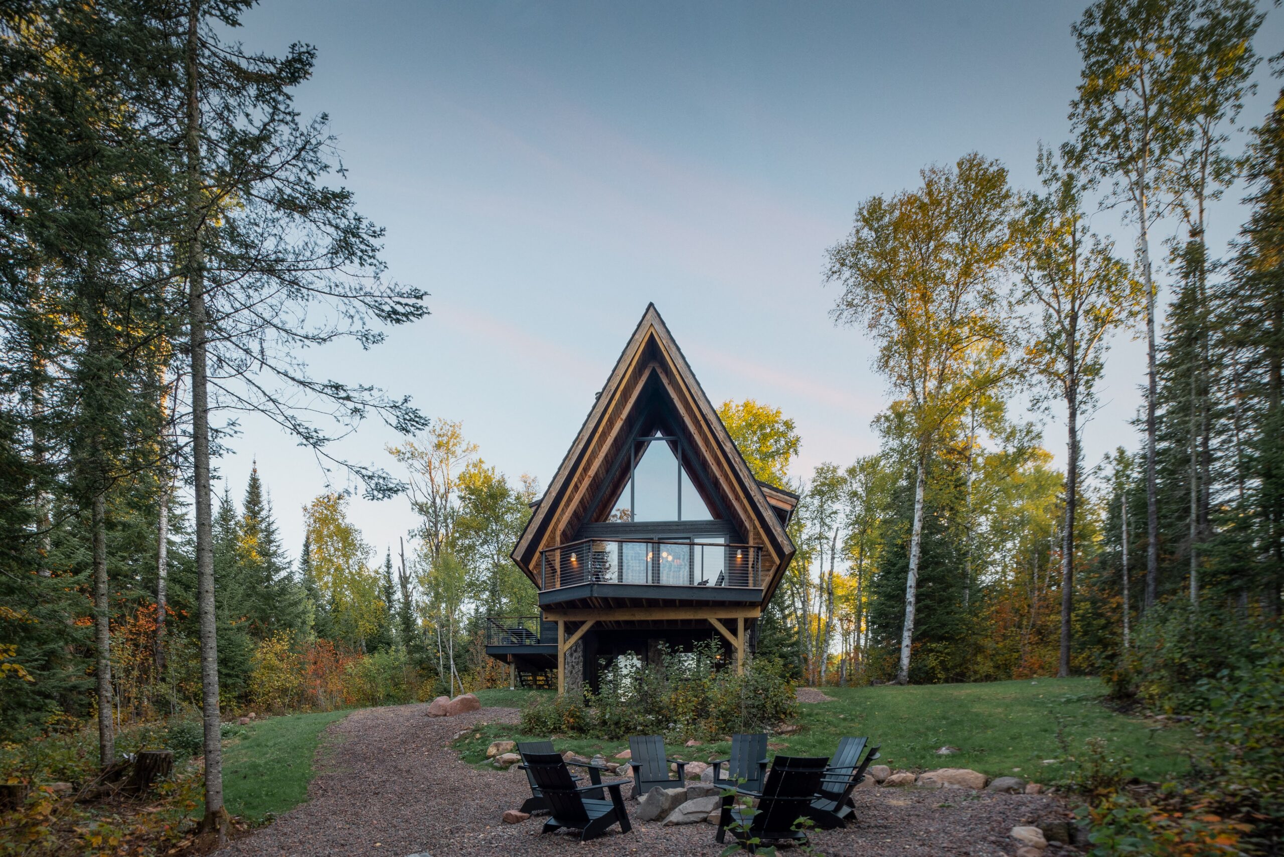 Outside wooded area view of The Minne Stuga Cabin in Grand Marais Minnesota at dusk prominently featuring Kebony modified wood siding throughout the houses' design